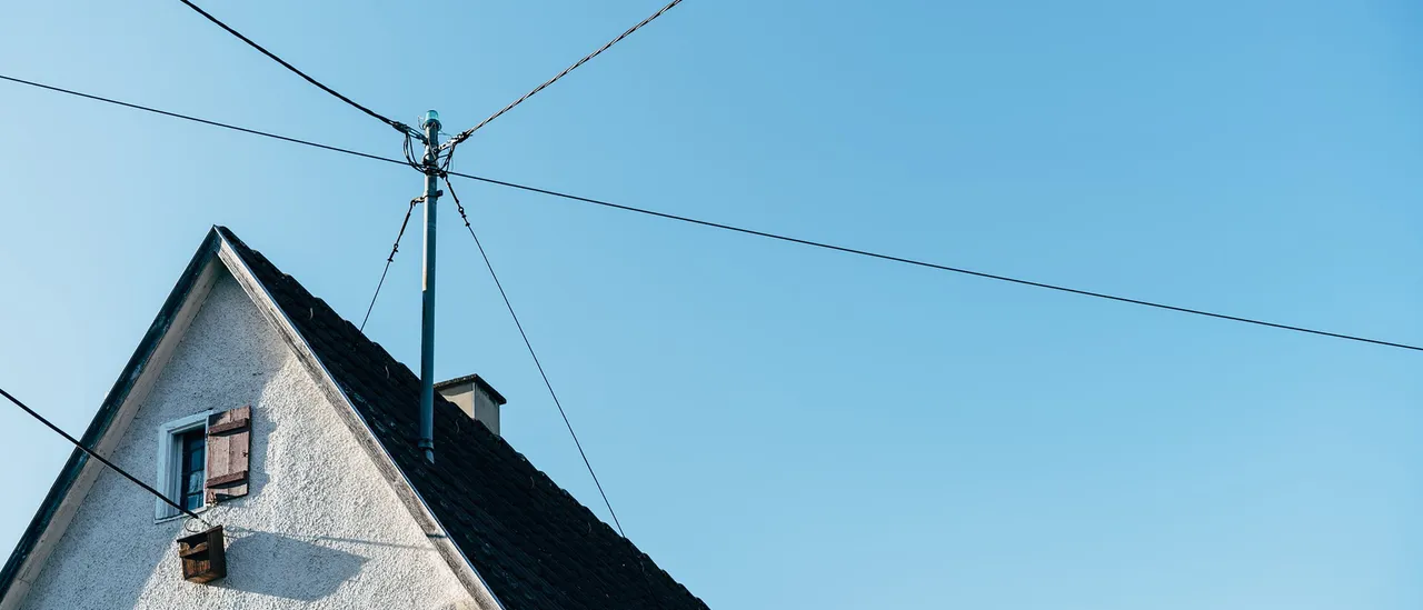 Overhead electric power lines converging at a rooftop service mast on a residential house against a clear blue sky