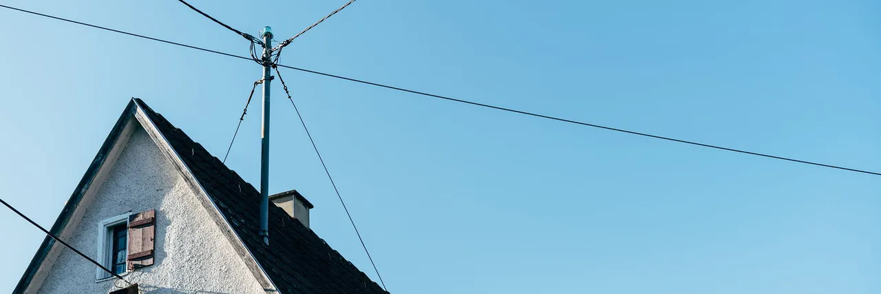 Overhead electric power lines converging at a rooftop service mast on a residential house against a clear blue sky