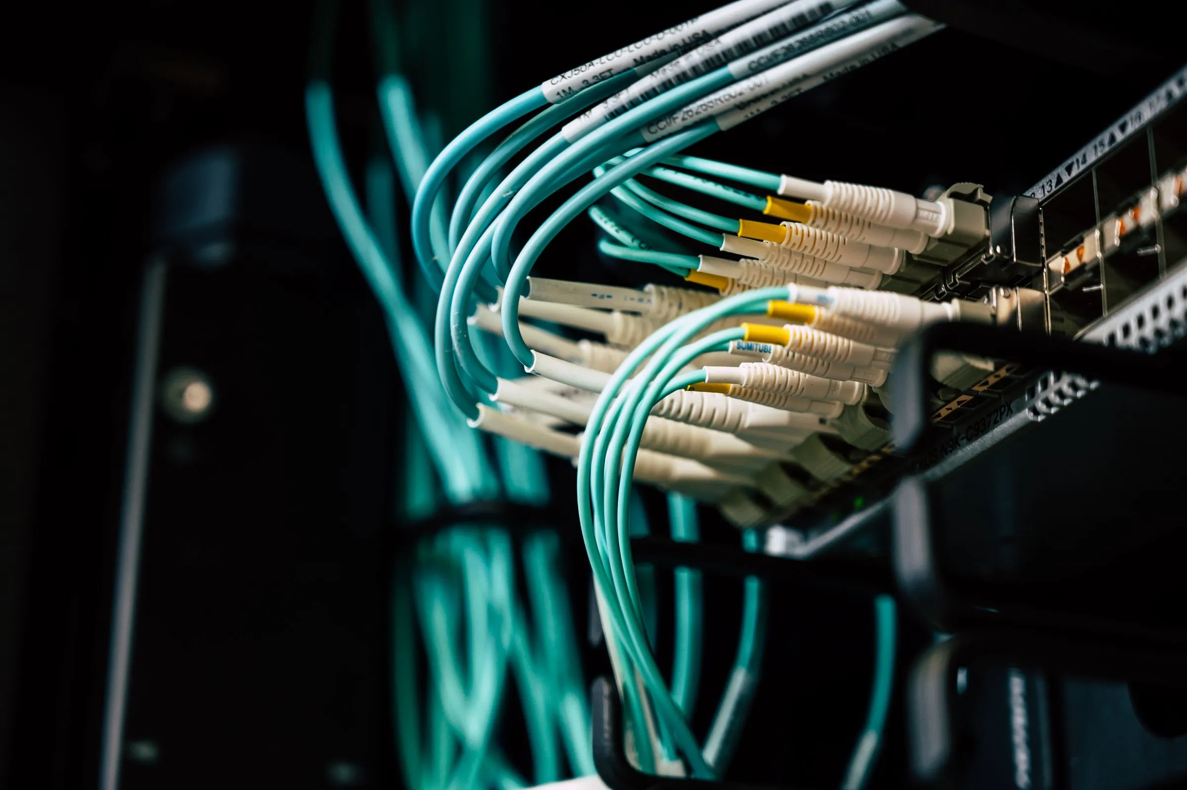 Close-up of dense teal fiber patch cables curving into the ports of a rack-mounted network switch in a dark data center