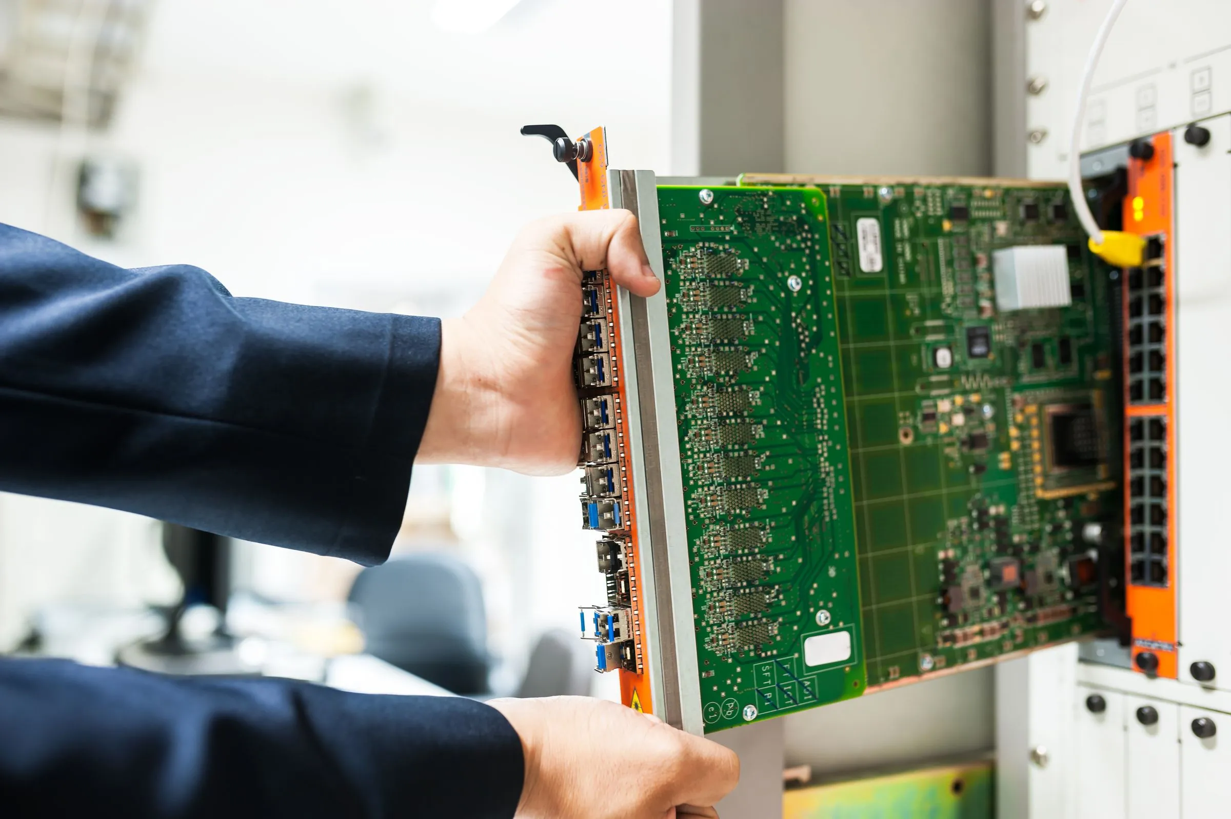 A technician’s hands sliding a green circuit board line card with optical ports into a network equipment chassis