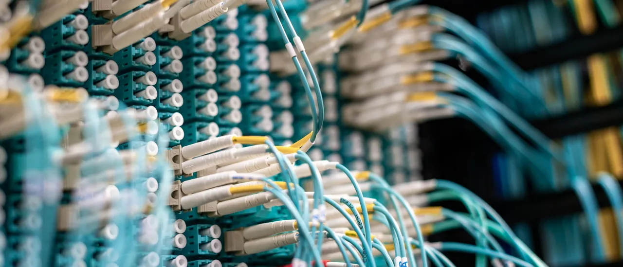 Dense bundles of teal fiber optic patch cables plugged into rows of connectors on data center patch panels
