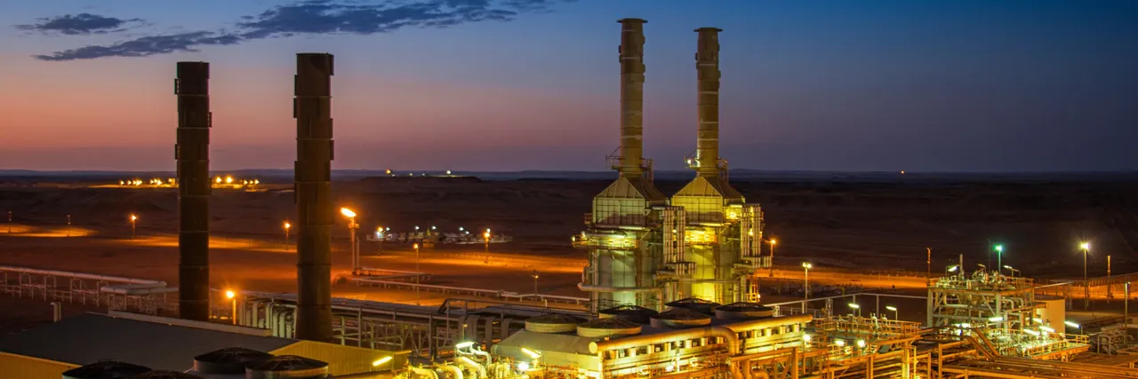 Gas-fired power facility with tall exhaust stacks and illuminated piping glowing at dusk under a deep blue sky