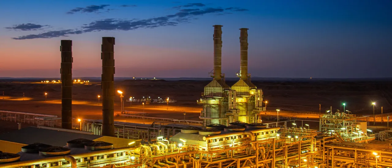 Gas-fired power facility with tall exhaust stacks and illuminated piping glowing at dusk under a deep blue sky