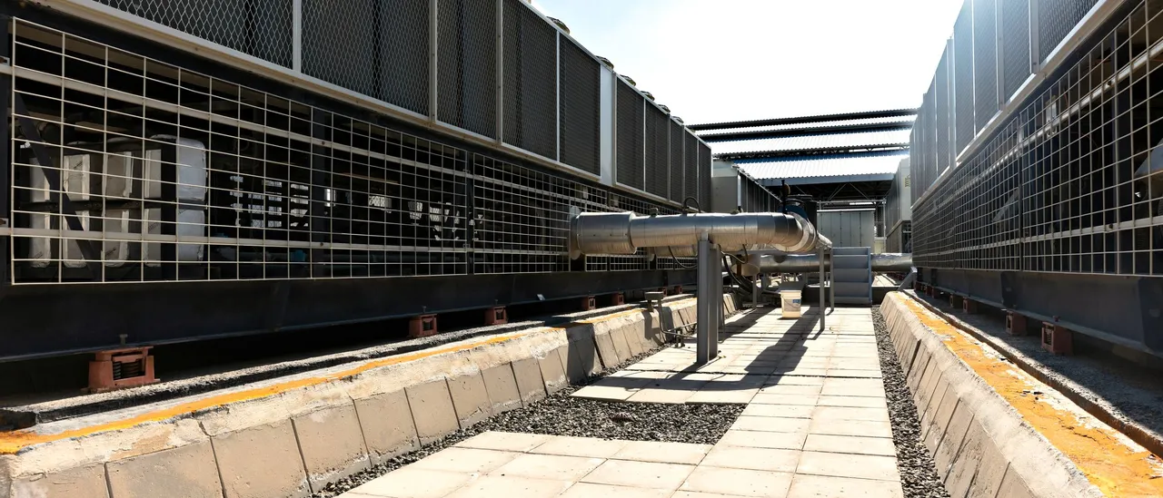 Rows of industrial cooling units and ductwork outdoors under a clear sky
