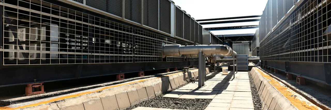 Rows of industrial cooling units and ductwork outdoors under a clear sky