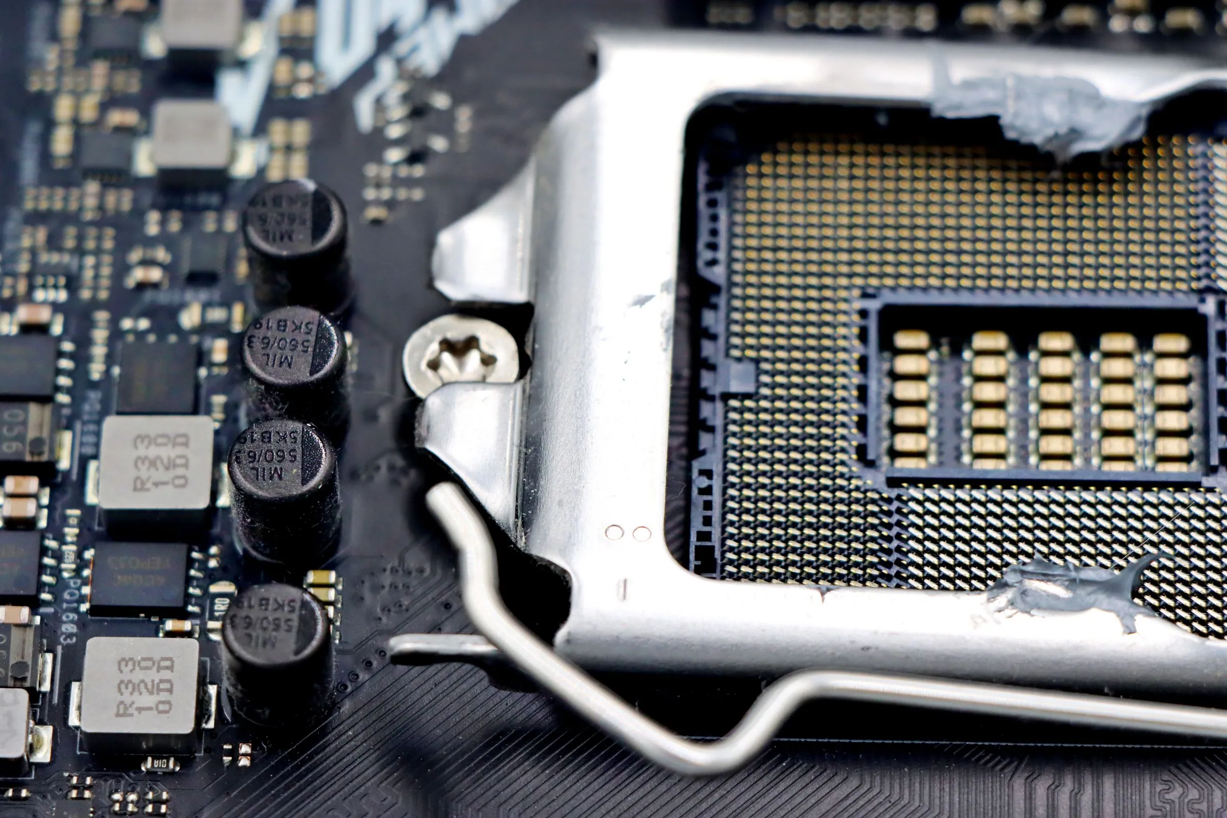 Close-up of an open CPU socket on a motherboard, showing the grid of gold contact pads, retention bracket, and surrounding capacitors