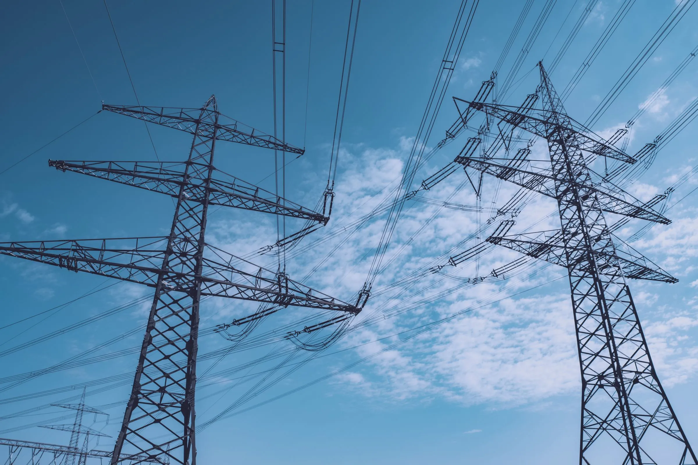 Two steel lattice transmission towers seen from below against a blue sky, their crossarms carrying bundled high-voltage conductors and strings of insulators