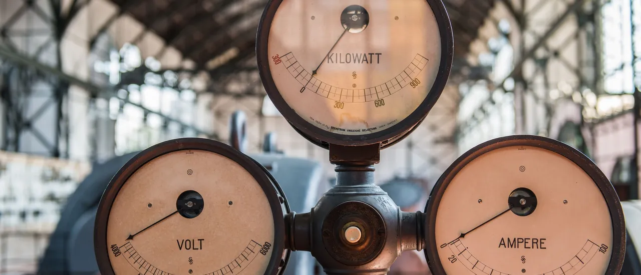 Three vintage analog gauges labeled kilowatt, volt, and ampere in an old industrial power hall