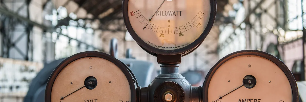 Three vintage analog gauges labeled kilowatt, volt, and ampere in an old industrial power hall