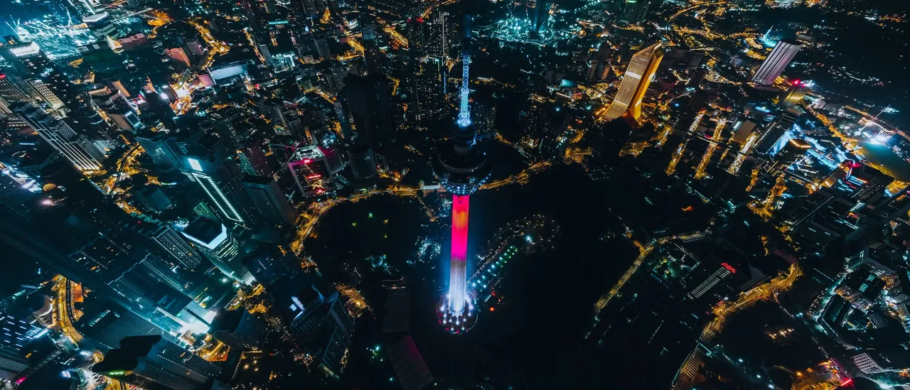 Aerial night view of Kuala Lumpur, Malaysia, with the illuminated KL Tower rising above a dense grid of city lights