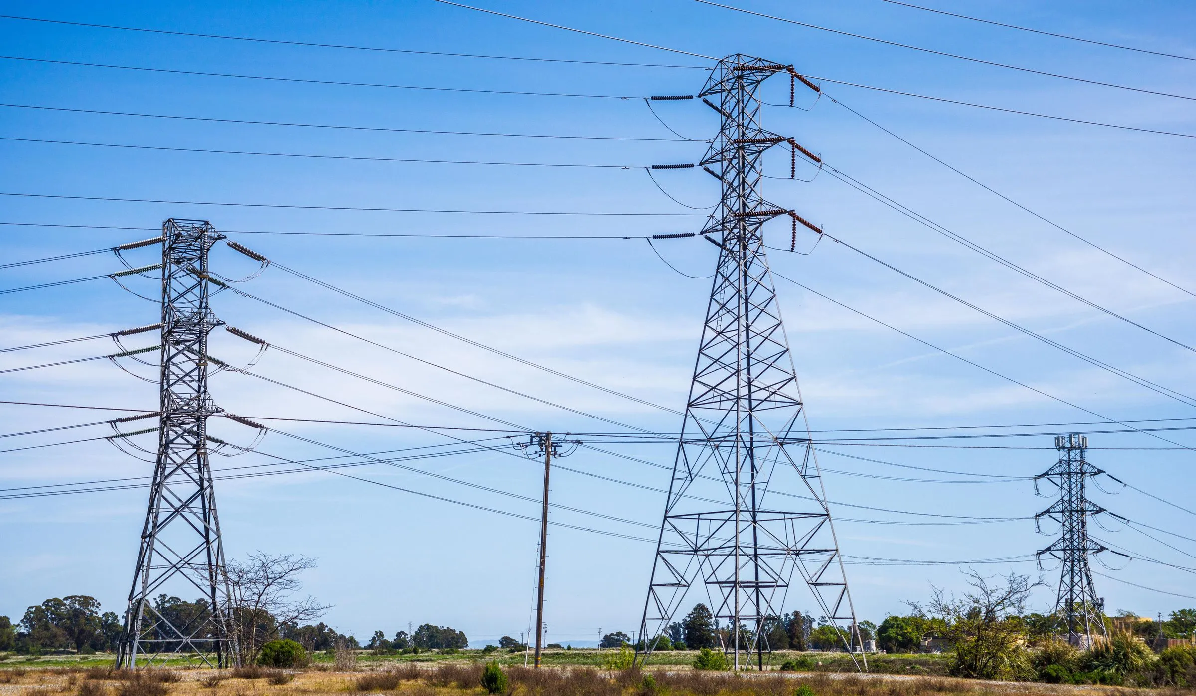 High-voltage transmission towers carrying power lines across open countryside under a blue sky