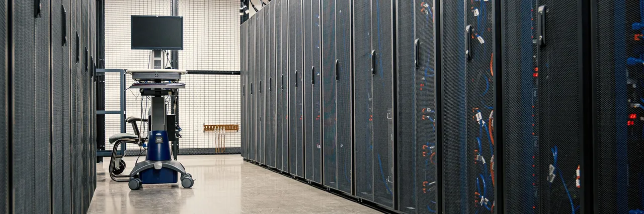 Rows of server racks lining a data hall aisle, with a monitoring cart at the far end