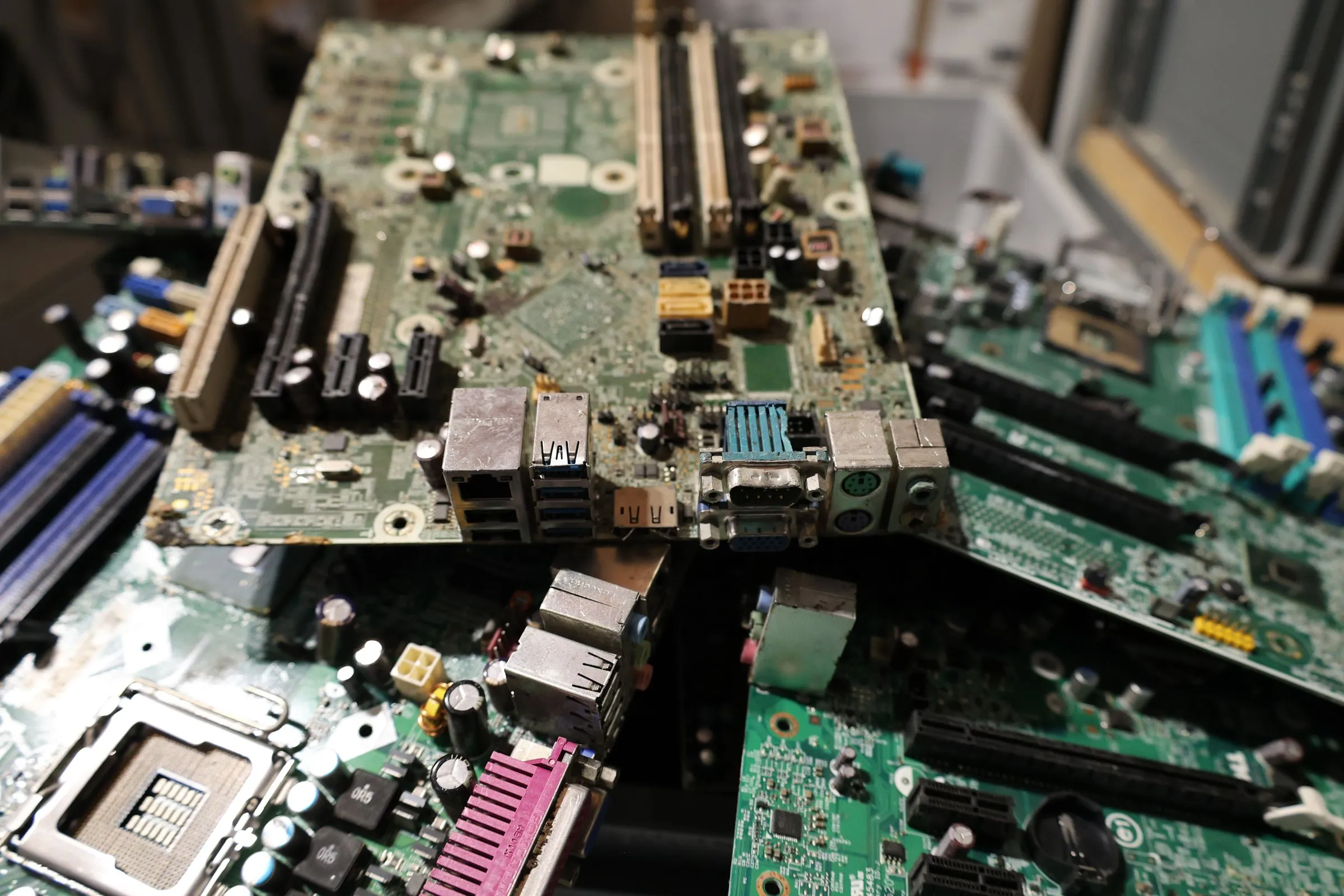 A pile of stripped green motherboards stacked at odd angles, their ports and empty CPU sockets exposed, waiting to be recycled
