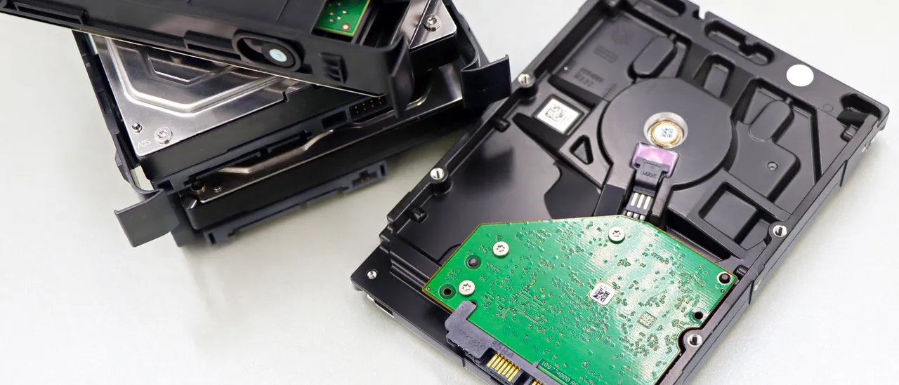 A stack of decommissioned bare hard disk drives on a white surface, one flipped to show its green circuit board and connectors