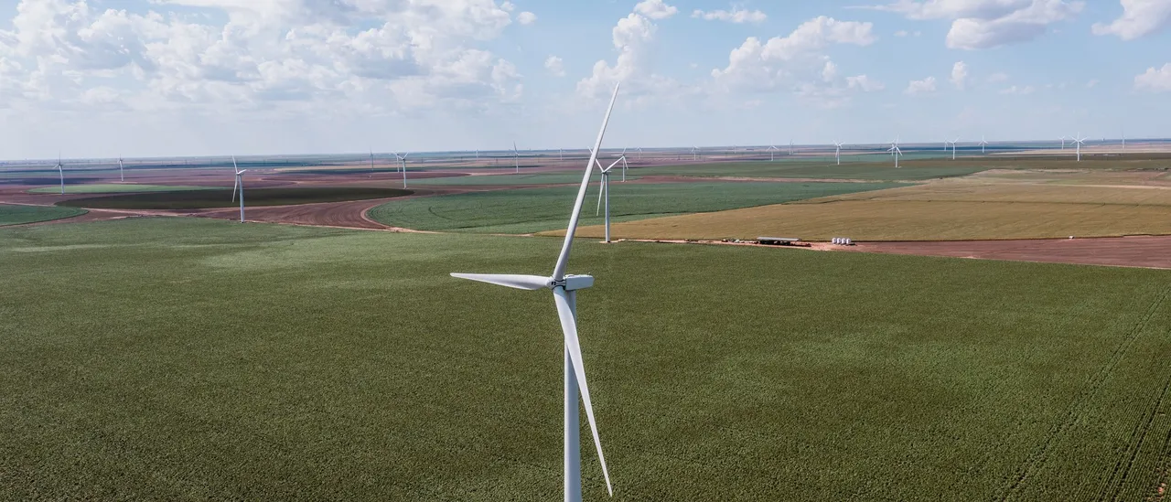 Aerial view of a wind farm near Groom in Carson County, Texas, with white turbines standing in green crop fields that stretch flat to the horizon under scattered clouds