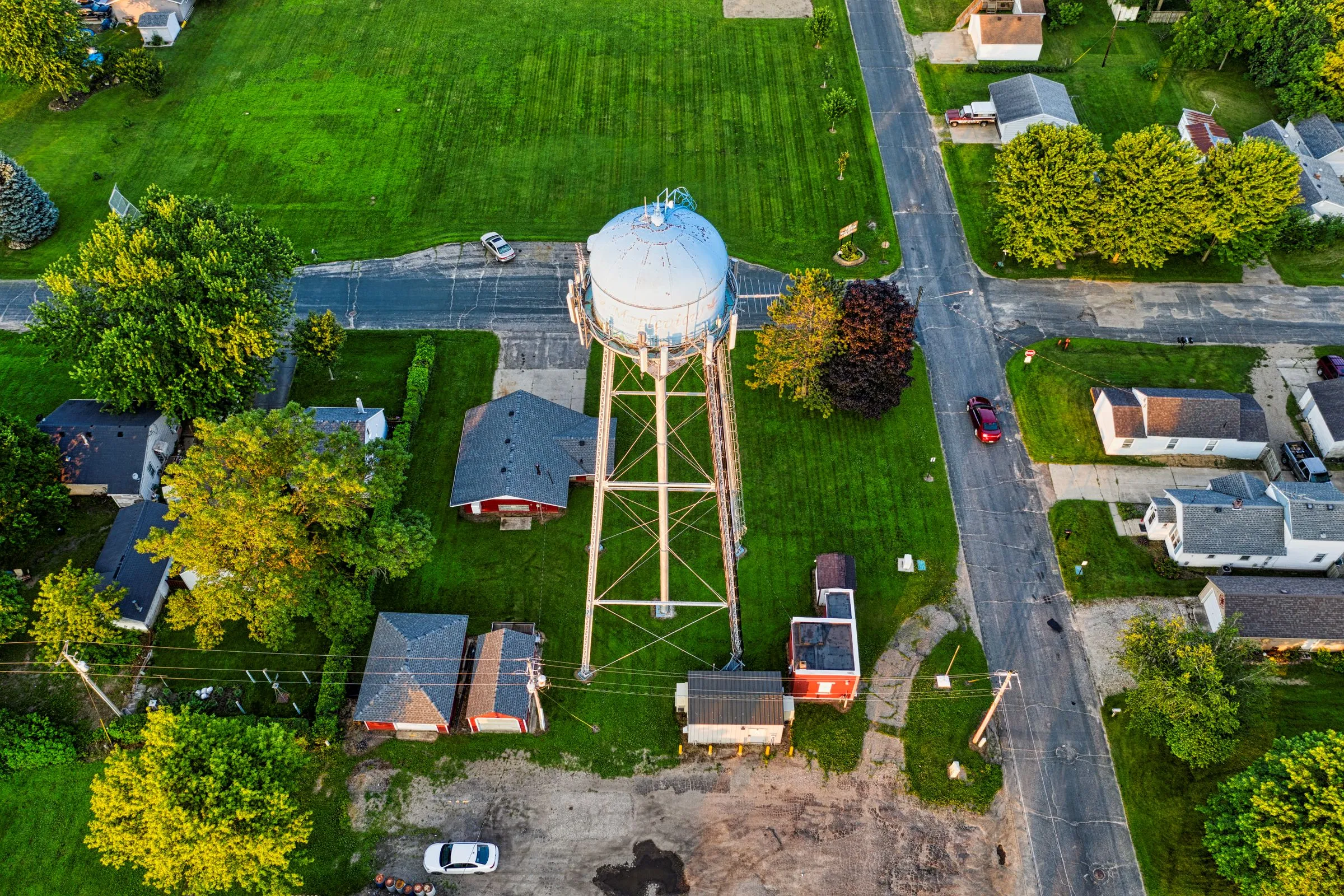 Aerial view of a municipal water tower rising above lawns, streets, and homes in a small Midwestern town