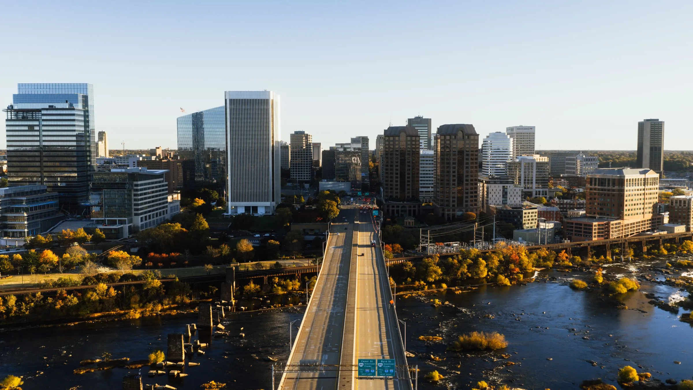 Aerial view of downtown Richmond, Virginia at dusk, with the Manchester Bridge crossing the James River, fall foliage along the banks, and office towers catching the last light