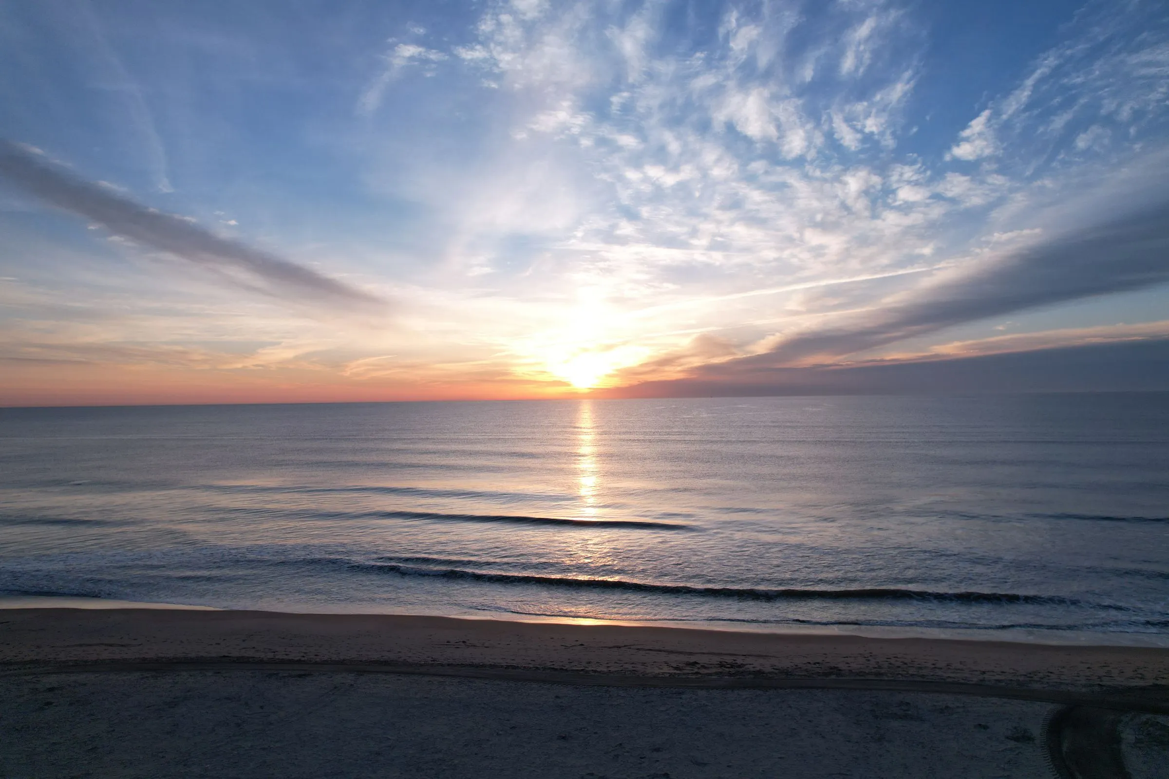 Sunrise over the Atlantic at the Virginia Beach oceanfront, with gentle waves rolling onto the sand under streaks of high cloud
