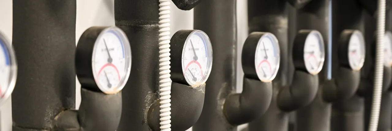 Row of black insulated pipes fitted with round temperature gauges in a heating plant room