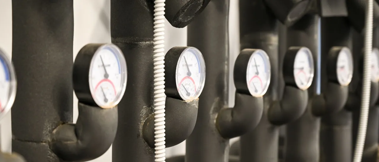 Row of black insulated pipes fitted with round temperature gauges in a heating plant room