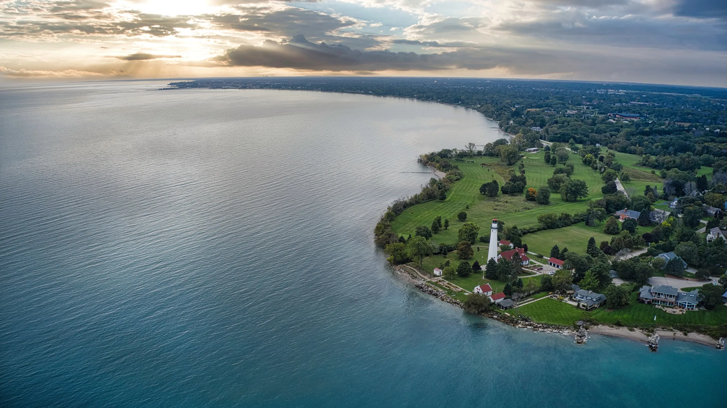 Aerial view of the Wind Point Lighthouse on a green point of land jutting into Lake Michigan north of Racine, Wisconsin, with the shoreline curving toward the horizon