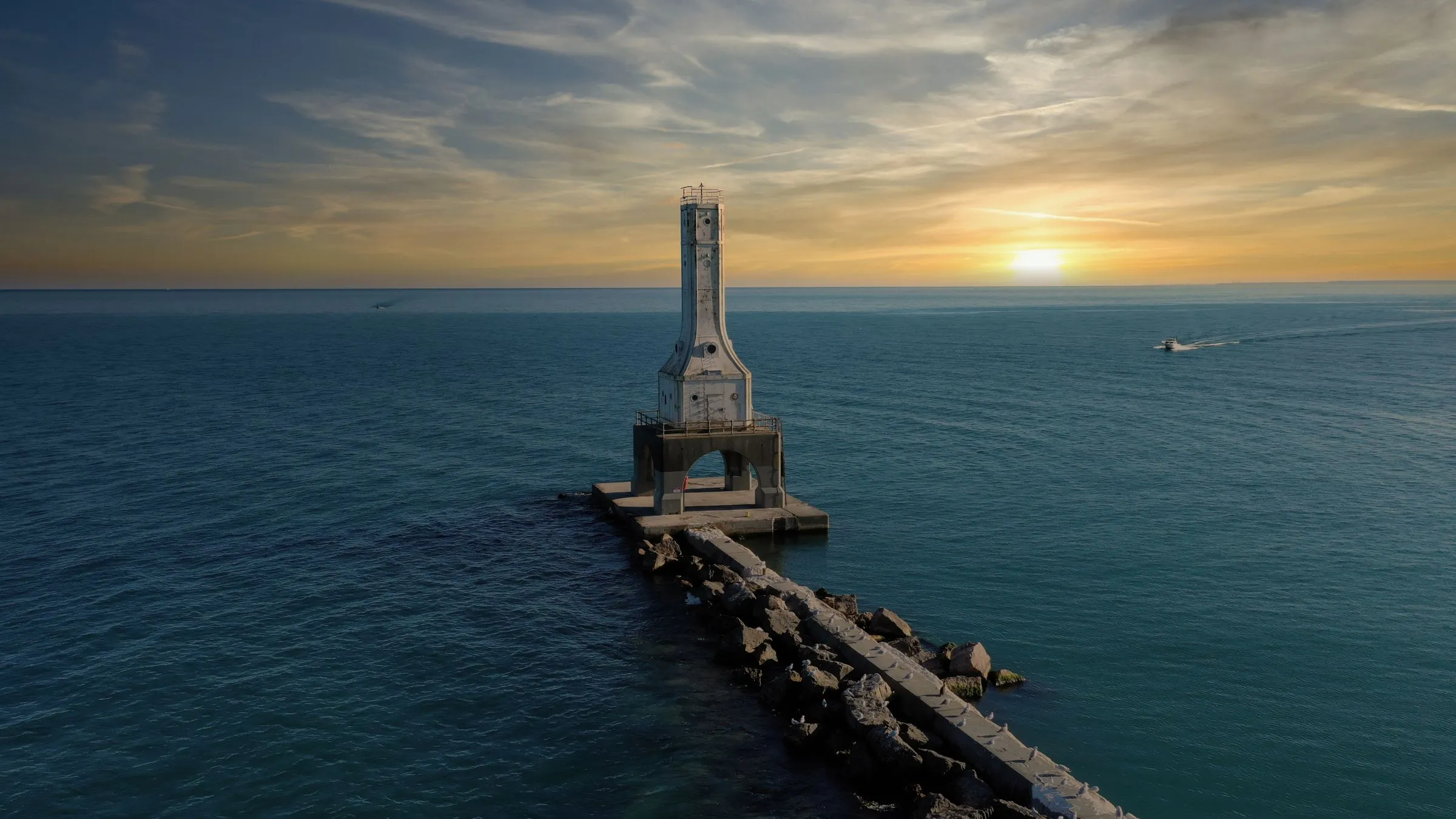 Aerial view of the Port Washington breakwater lighthouse on Lake Michigan at sunrise, with a small boat passing offshore