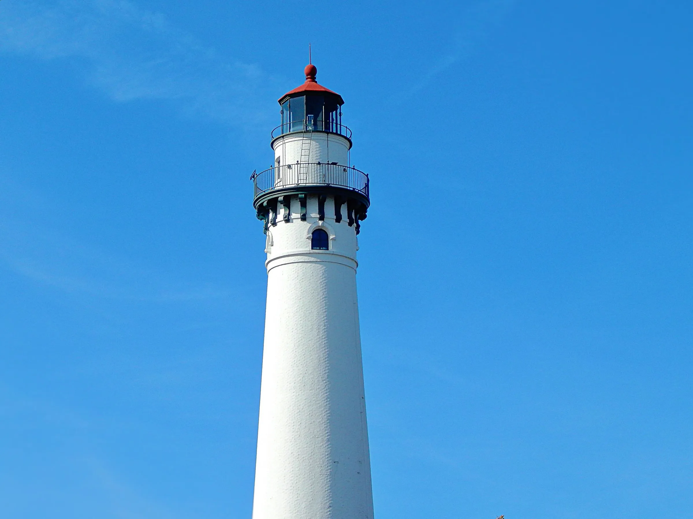 The white brick tower of Wind Point Lighthouse in Racine County, Wisconsin, with its red lantern room and black iron gallery against a clear blue sky
